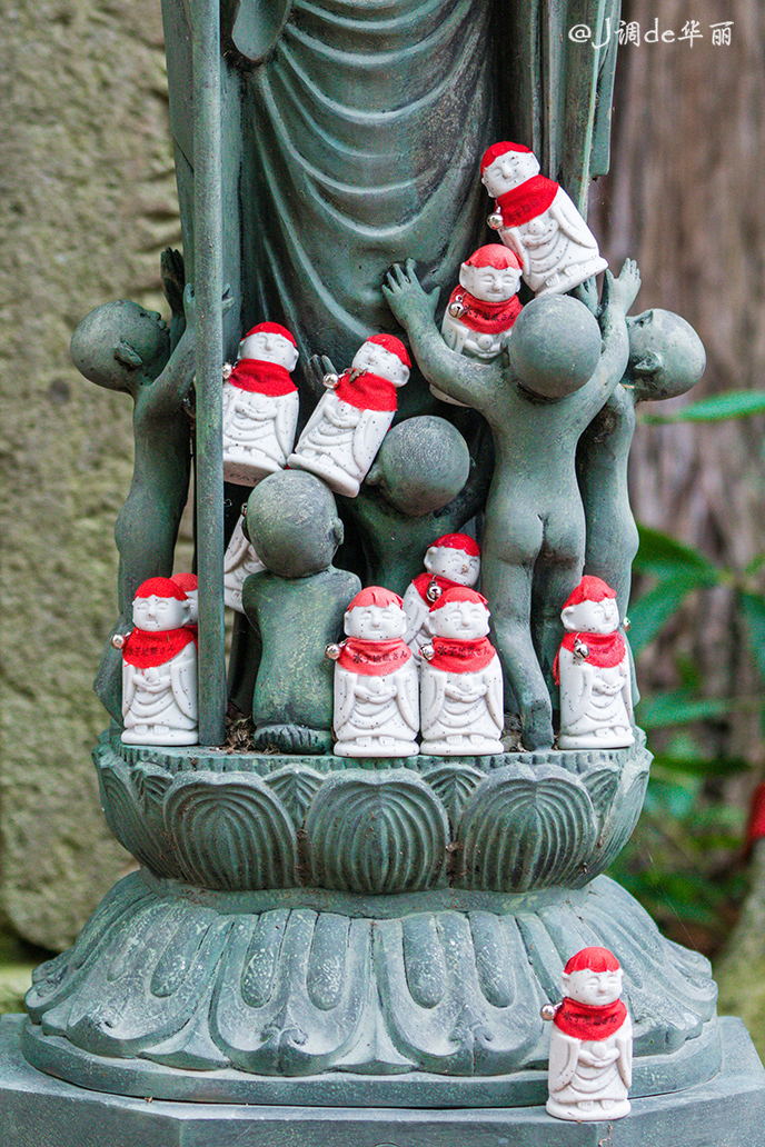 很多白色的瓷娃娃,脖子挂着铃铛和红色的围布,上面写着"水子地藏さん"